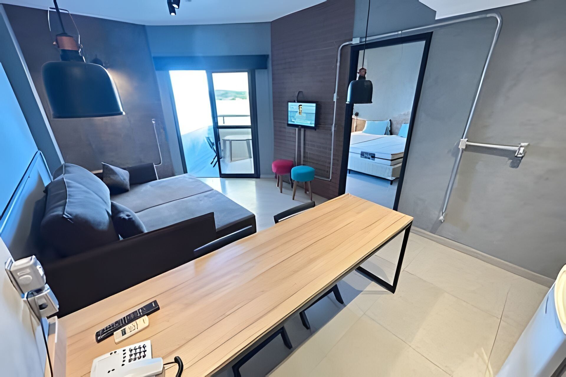 Quarto de hotel moderno com sofá, mesa de madeira, televisão e varanda com vista.