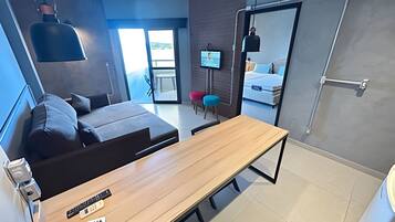 Quarto de hotel moderno com sofá, mesa de madeira, televisão e varanda com vista.