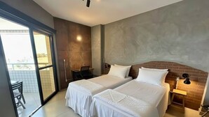 A hotel room with two beds, a brick accent wall, a small table, and a sliding glass door to the balcony. - SHB Magia de uma Vista Panorâmica (Santos)