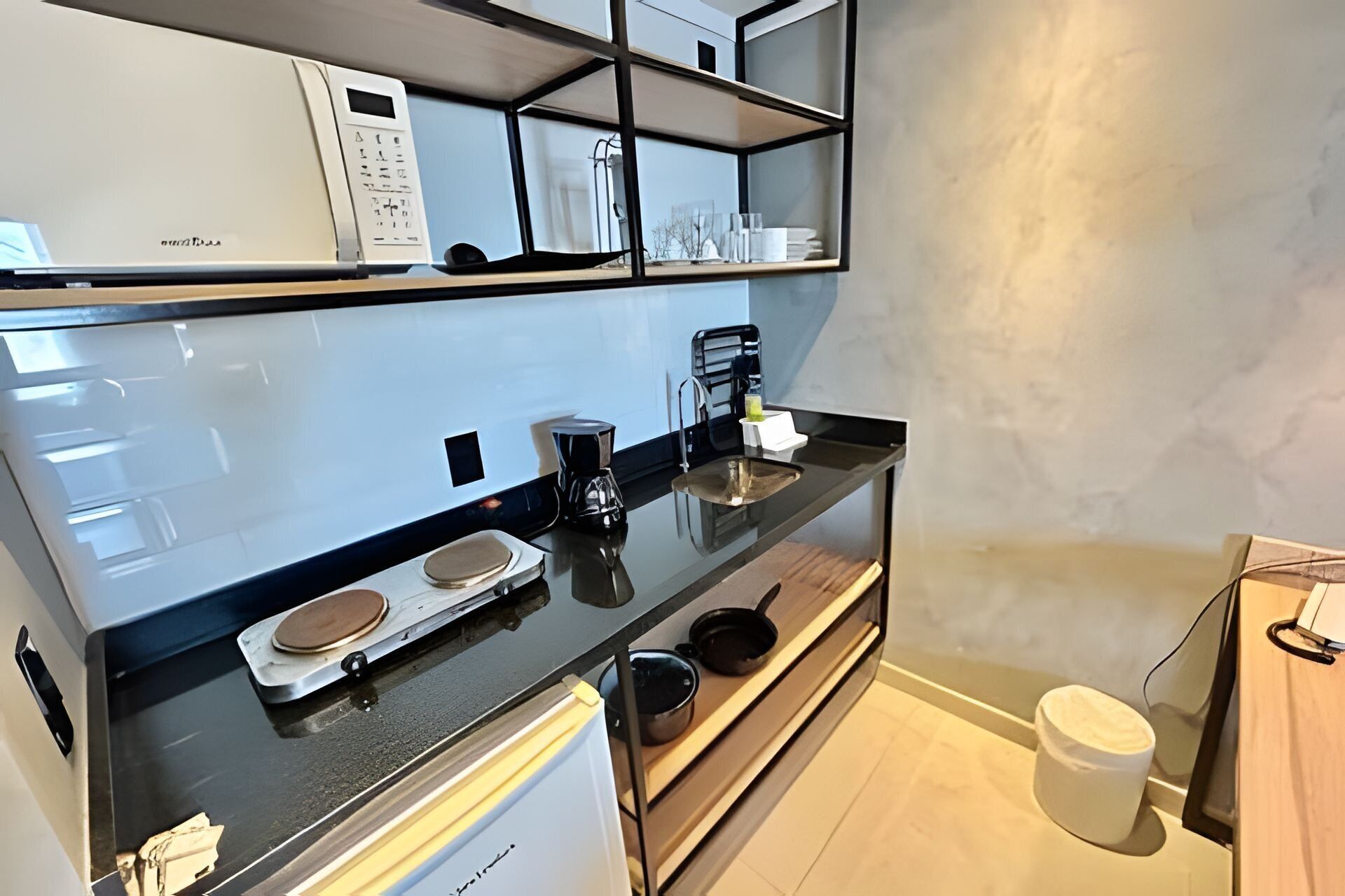 Una cocina moderna con encimera negra, electrodomésticos blancos y un estante empotrado sobre el fregadero.