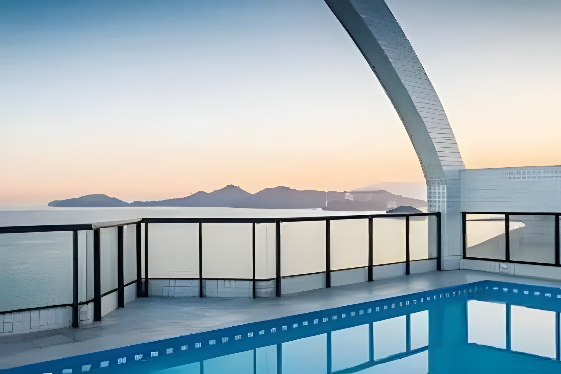 Un área de piscina moderna con vista despejada al mar y montañas a lo lejos.