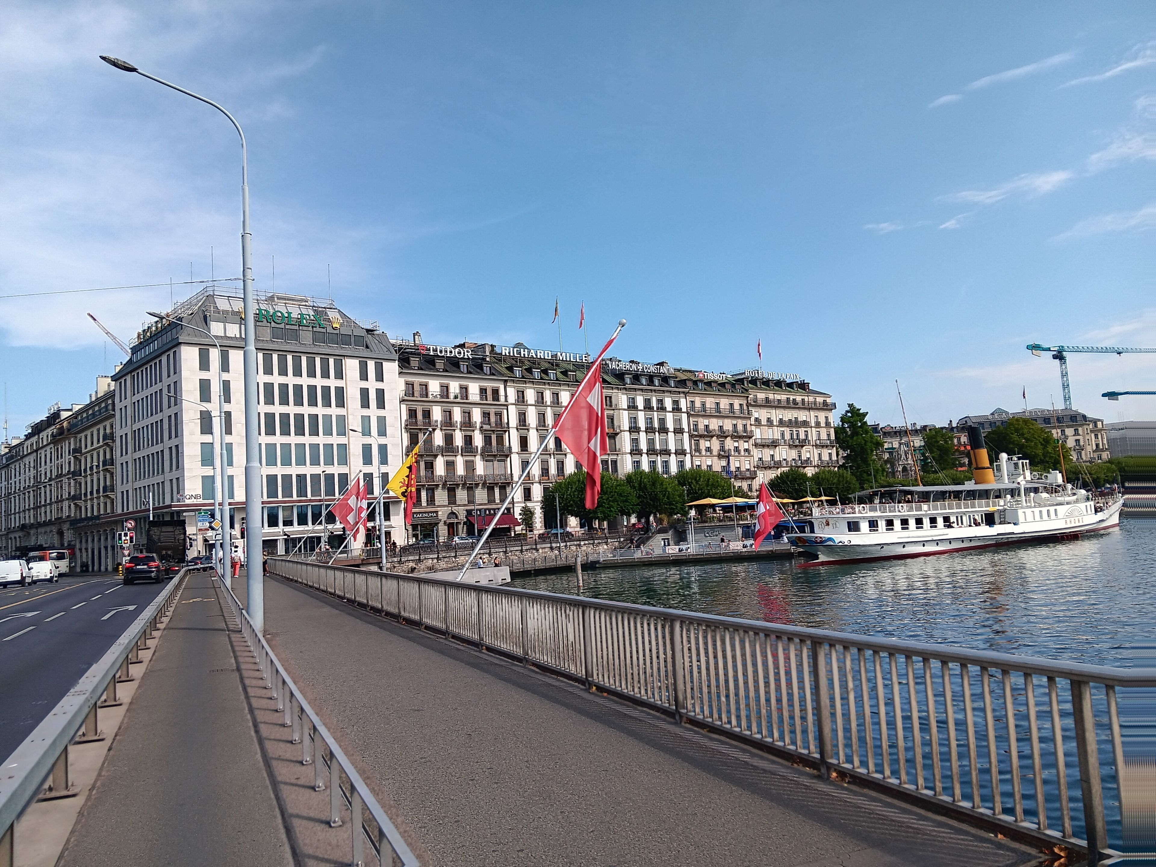 Ein Hotel am Wasserufer mit mehreren Stockwerken, einem Fluss und einer Fußgängerbrücke.