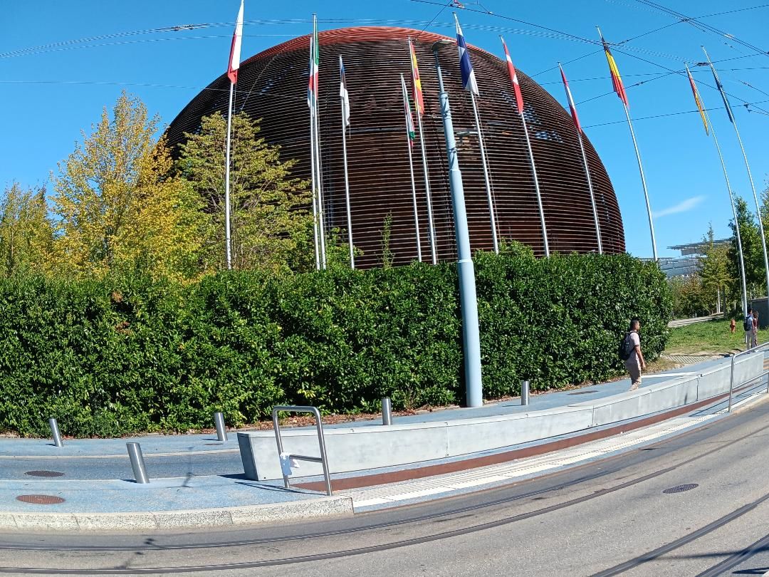 Ein modernes Gebäude mit einer geschwungenen Fassade, umgeben von einer niedrigen Hecke und einem Bürgersteig.