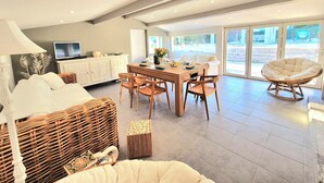 Una sala de estar moderna con comedor, televisor y un amplio ventanal con vistas al exterior.