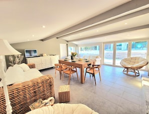 Ein modernes Wohnzimmer mit Essbereich, einem Fernseher und einem großen Fenster mit Blick ins Freie.