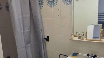 Une salle de bain avec un rideau de douche, un lavabo, un miroir et une étagère contenant des articles de toilette.