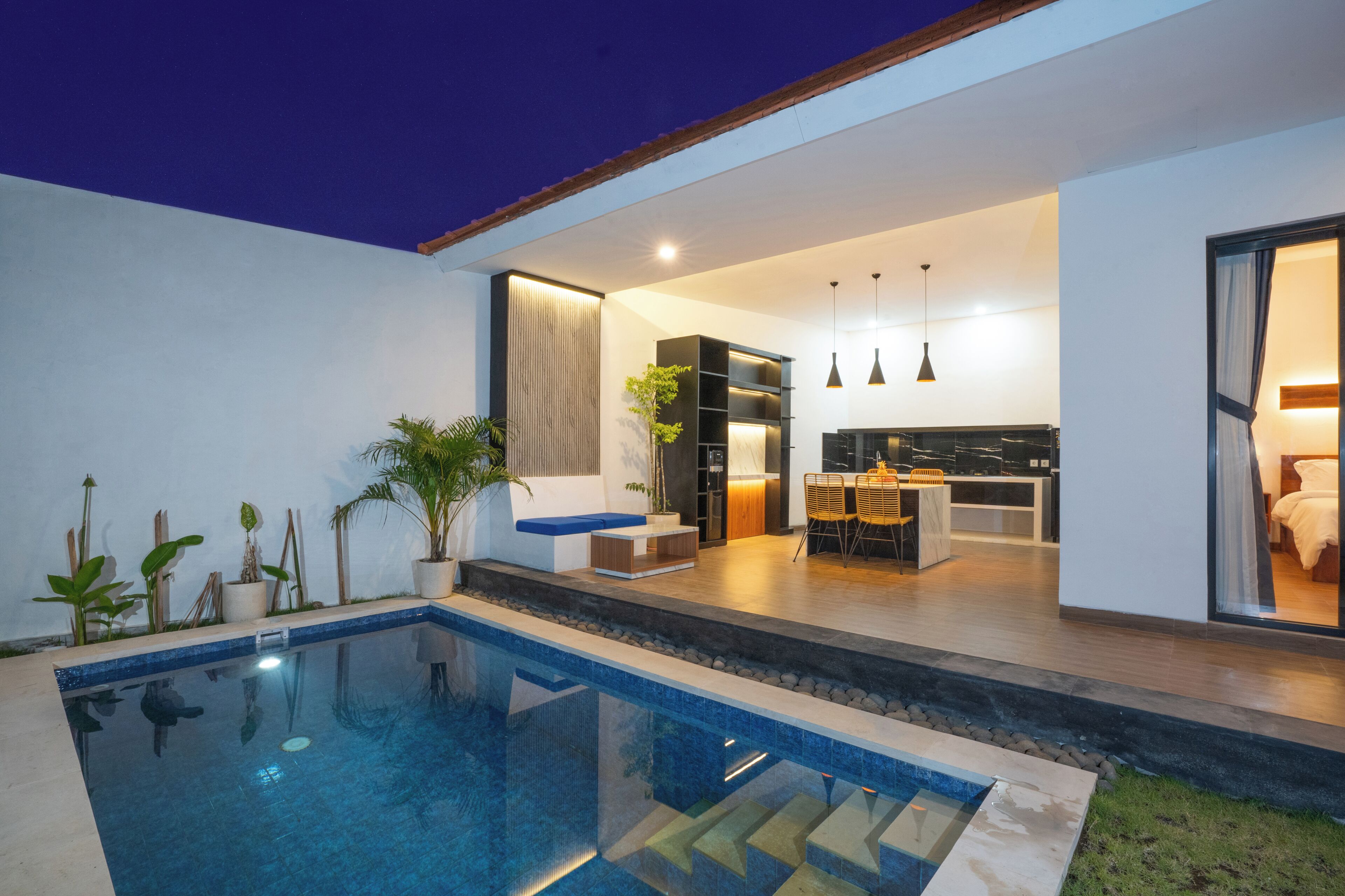 A modern outdoor pool area with a dining space and a kitchen visible through an open door.