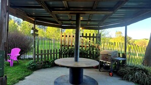Un espacio al aire libre cubierto con una mesa y una parrilla, rodeado por una valla de madera y follaje.