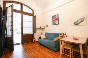An open door leading outside, a blue sofa, a small table with a bowl, and a colorful abstract painting on the wall. - Turin City Centre | Mazzini 39 House (Torino)