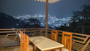 A balcony with a table and chairs, overlooking a cityscape at night. - Twin Garden by TAPSOM (Gangtok)