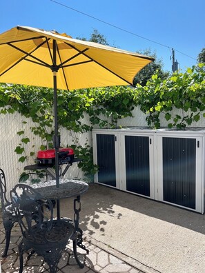 A patio area with a table and chairs, a yellow umbrella, and a white fence with green vines.