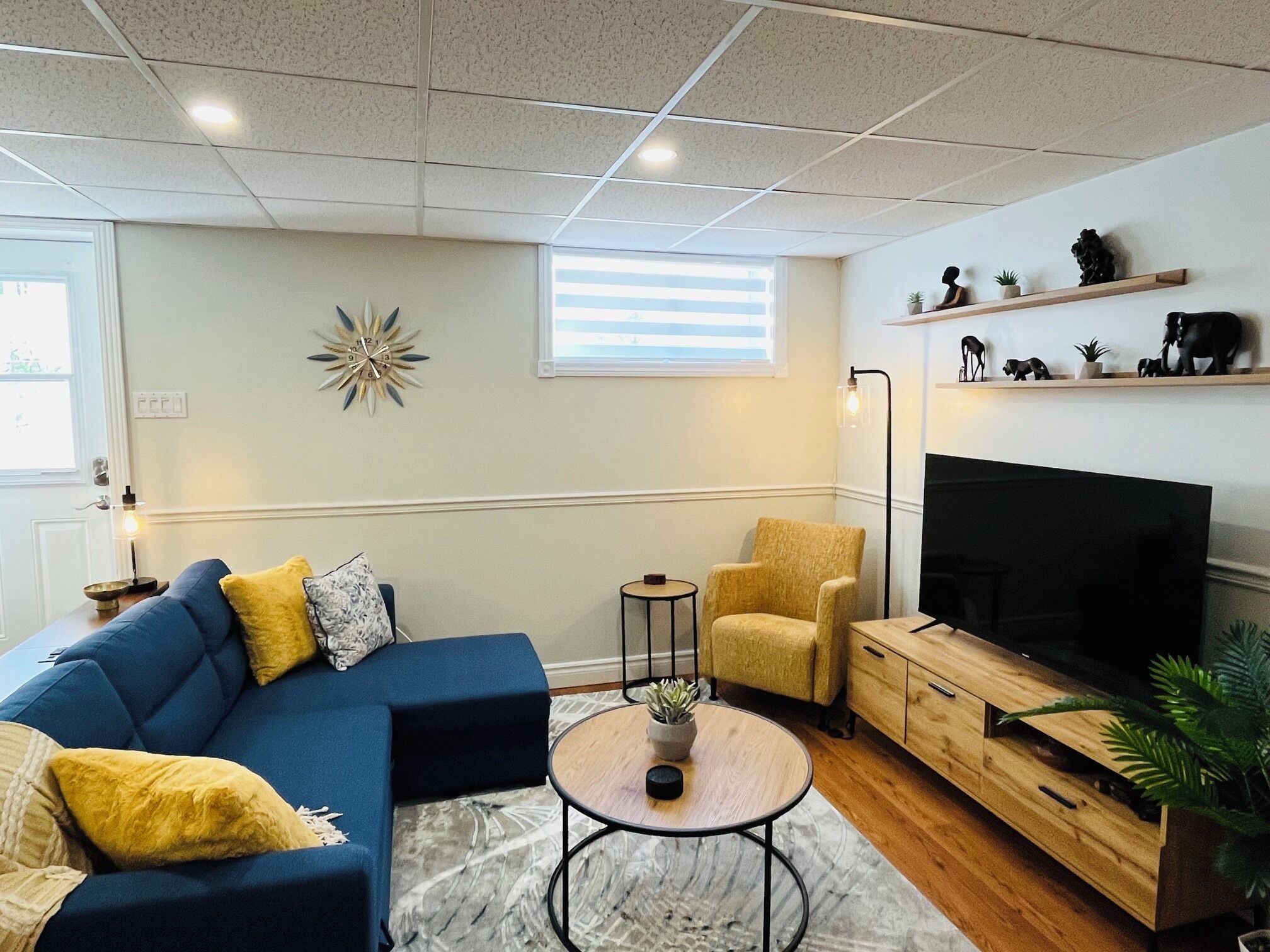 A living room with a sofa, armchair, coffee table, TV, and decorative items on shelves.