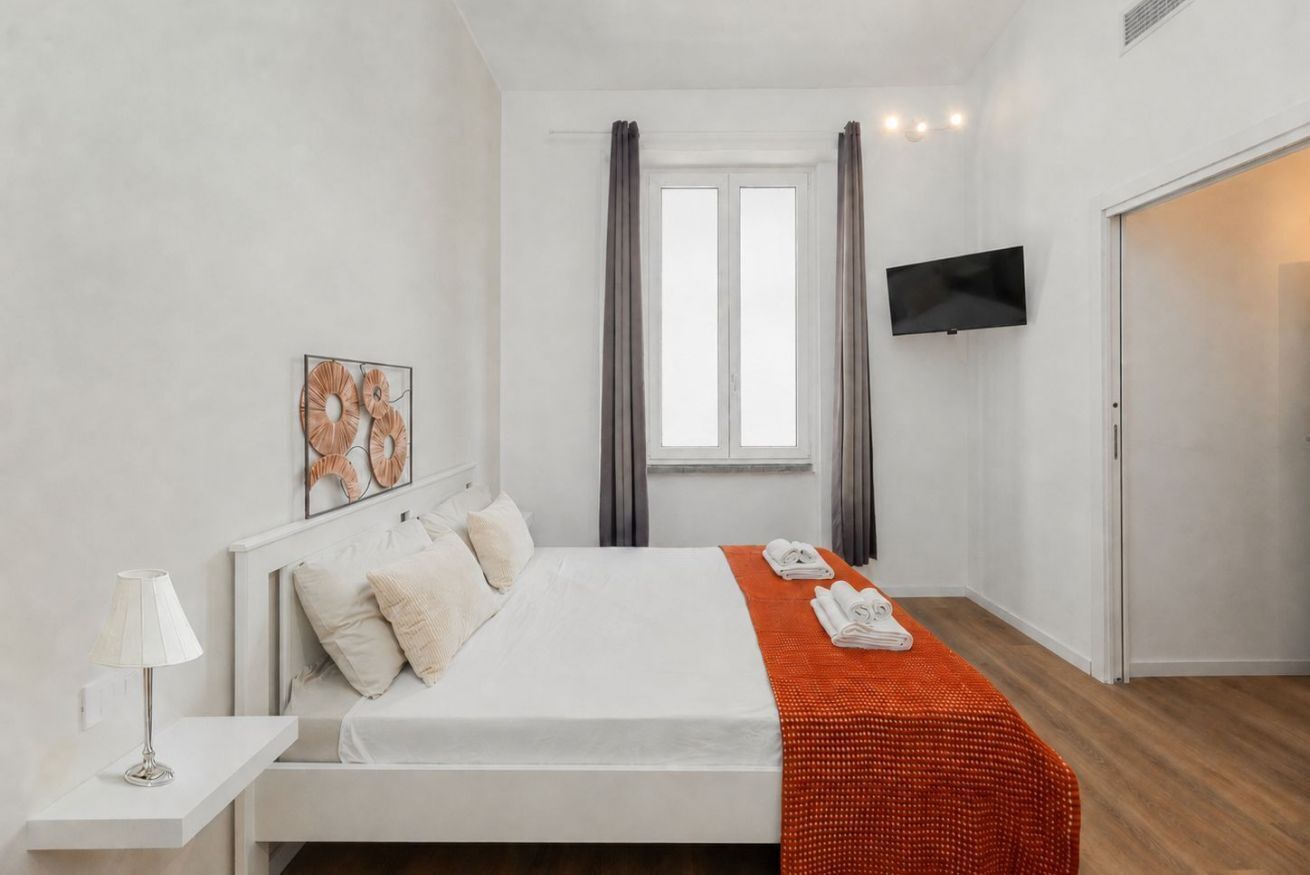 Une chambre d’hôtel comprenant un lit, un téléviseur à écran plat, une fenêtre avec des rideaux et une œuvre d’art accrochée au mur.