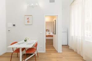 Een moderne eetruimte met een witte tafel, oranje stoelen en een ingelijst kunstwerk aan de muur.