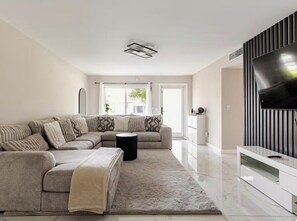 Ein modernes Wohnzimmer mit einem Ecksofa, einem Flachbildfernseher, einem Couchtisch und einem großen Fenster.