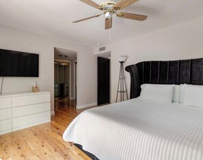Ein Schlafzimmer mit einem Bett, einem Deckenventilator, einem an der Wand montierten Fernseher und einer weißen Kommode.
