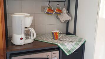 Una cocina con cafetera, microondas y una repisa con tazas y tetera.