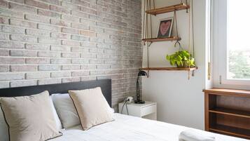 Una camera da letto con parete in mattoni, un letto con biancheria bianca, un comodino con una lampada e una finestra con vista.