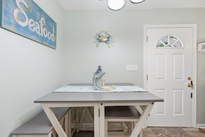 Uma área de refeições com mesa e bancos, um objeto decorativo na parede, uma porta com janela e um candeeiro fixado na parede.