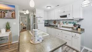 Une cuisine moderne avec des meubles blancs, un plan de travail en granit et un four à micro-ondes encastré.