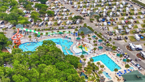 Vue aérienne d’un terrain de camping avec plusieurs camping-cars, une grande piscine et un toboggan aquatique.