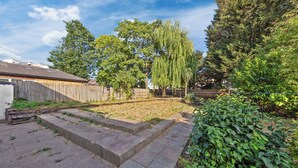 Un jardin avec une clôture en bois, une pelouse et divers arbres, dont un grand saule pleureur.