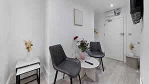 Une pièce moderne avec une table en marbre, deux chaises, un vase contenant des fleurs séchées et un tableau accroché au mur.