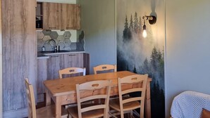 A dining area with a wooden table and chairs, a kitchen in the background, and a wall with a forest mural. - Renovated Apartment in Super Dévoluy with Heated Pool and Sauna (Dévoluy)