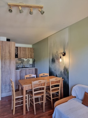 A dining area with a wooden table and chairs, a kitchen in the background, and a wall with a forest mural. - Renovated Apartment in Super Dévoluy with Heated Pool and Sauna (Dévoluy)