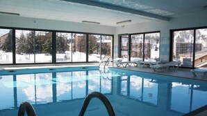 An indoor swimming pool with clear windows, lounge chairs, and a view of snowy mountains. - Renovated Apartment in Super Dévoluy with Heated Pool and Sauna (Dévoluy)