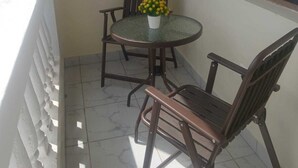 Een klein balkon met een ronde tafel, twee stoelen en een raam met tralies.