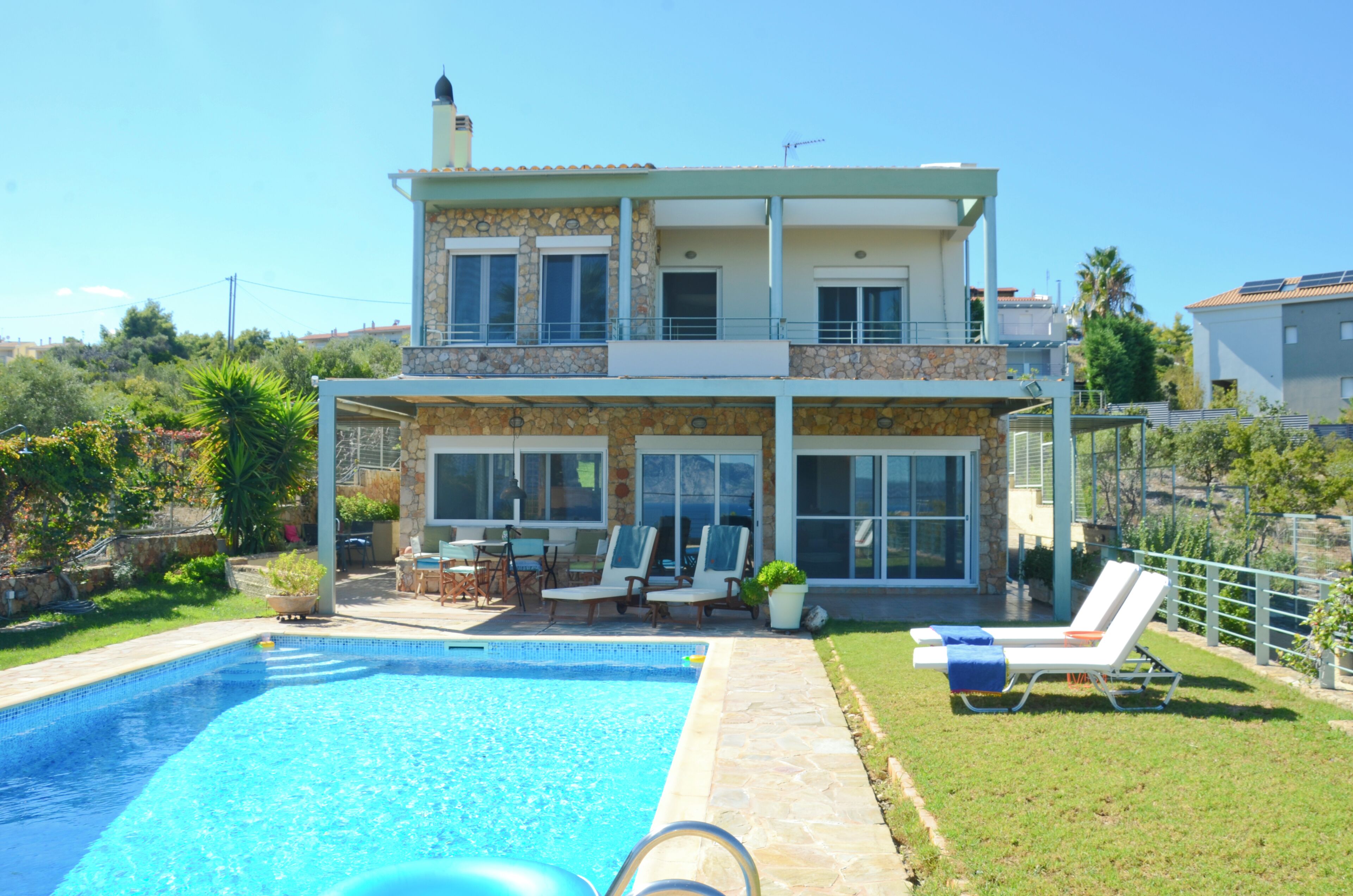 Une maison à deux étages avec une piscine, un espace salon extérieur et un balcon.