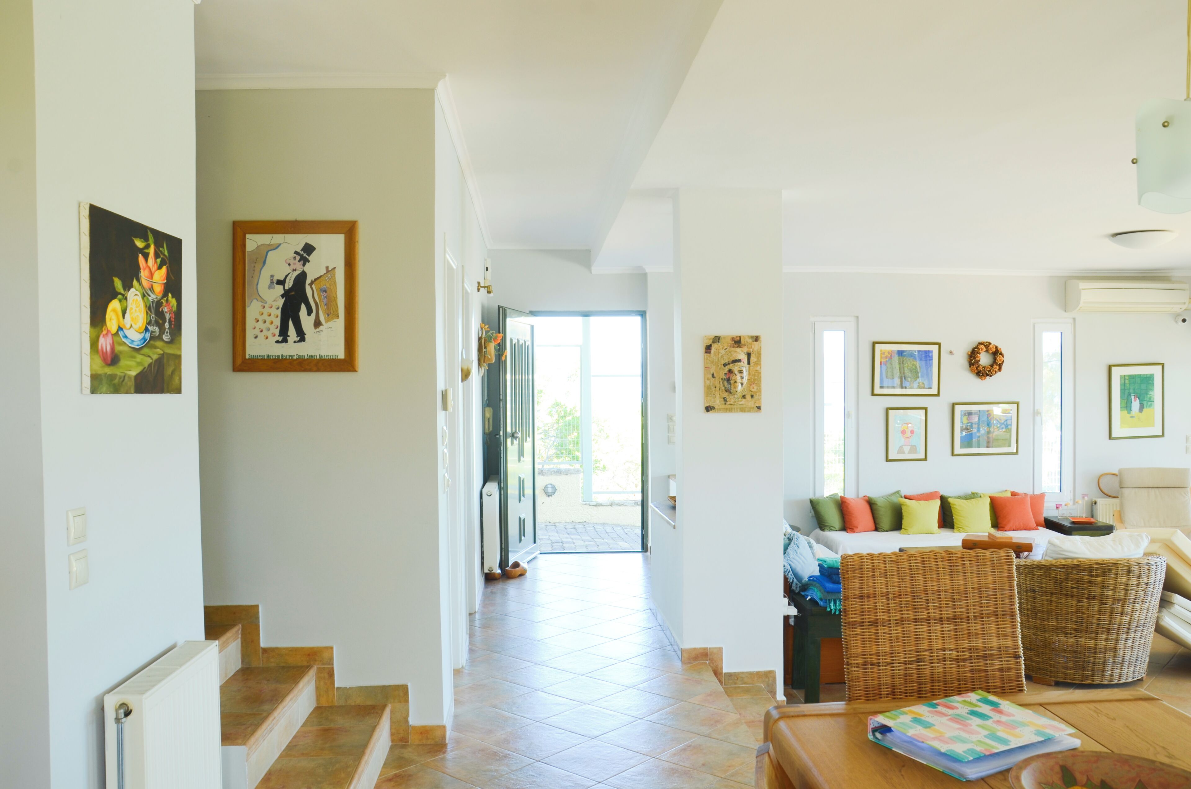 A spacious living area with a sofa, wicker chairs, a dining table, and a staircase leading to another room.