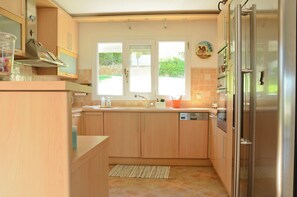 A modern kitchen with wooden cabinets, a stainless steel refrigerator, and a window overlooking a garden.