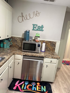 A kitchen with a microwave, coffee maker, and a dish rack. There are cabinets and a stainless steel dishwasher.