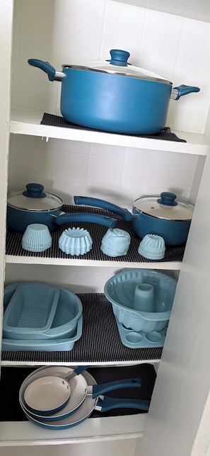 A kitchen with a blue pot on the top shelf, various kitchenware on the middle shelf, and a blue pan on the bottom shelf.