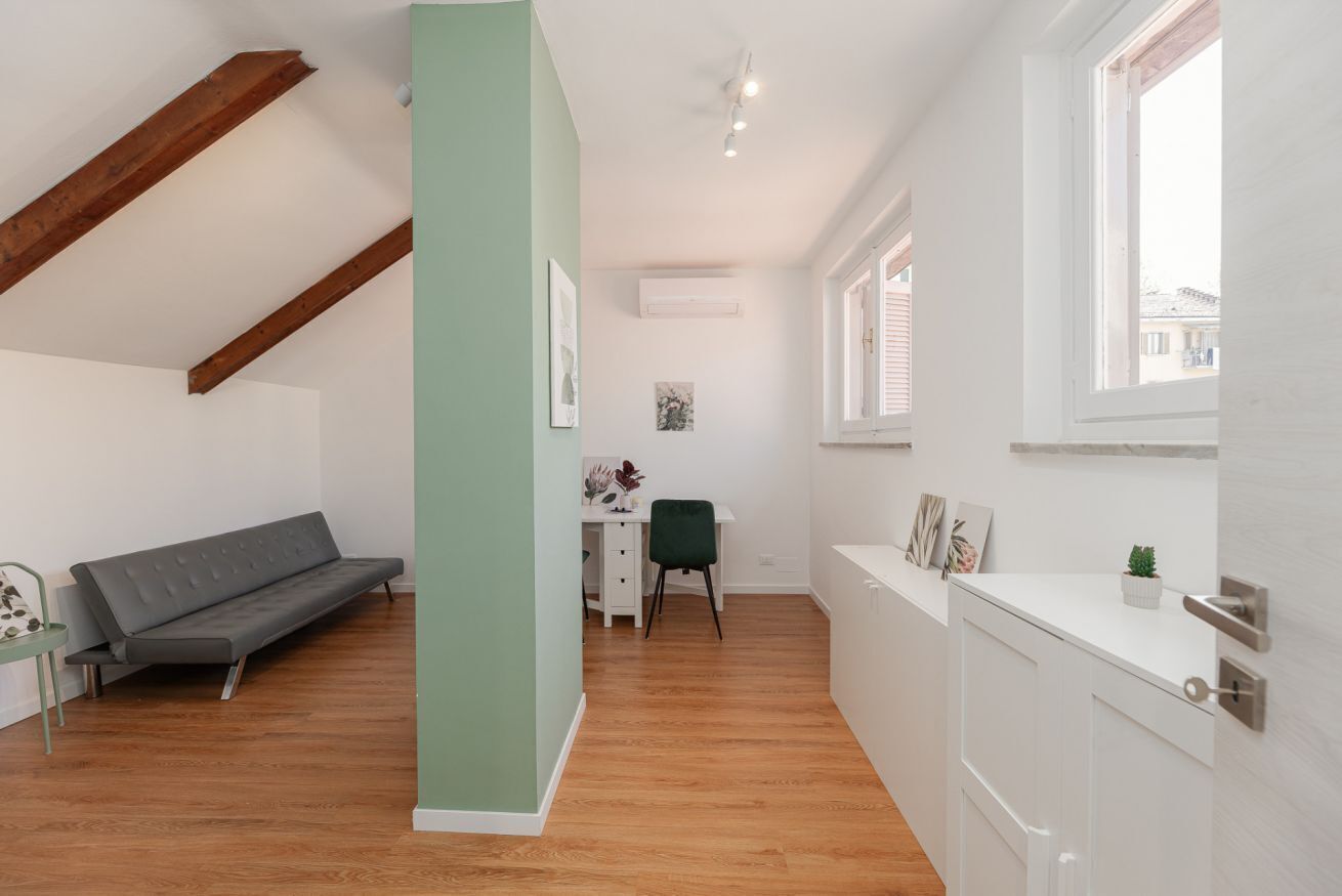 Une pièce avec un plancher en bois, un canapé gris, un bureau avec une chaise et un meuble blanc.