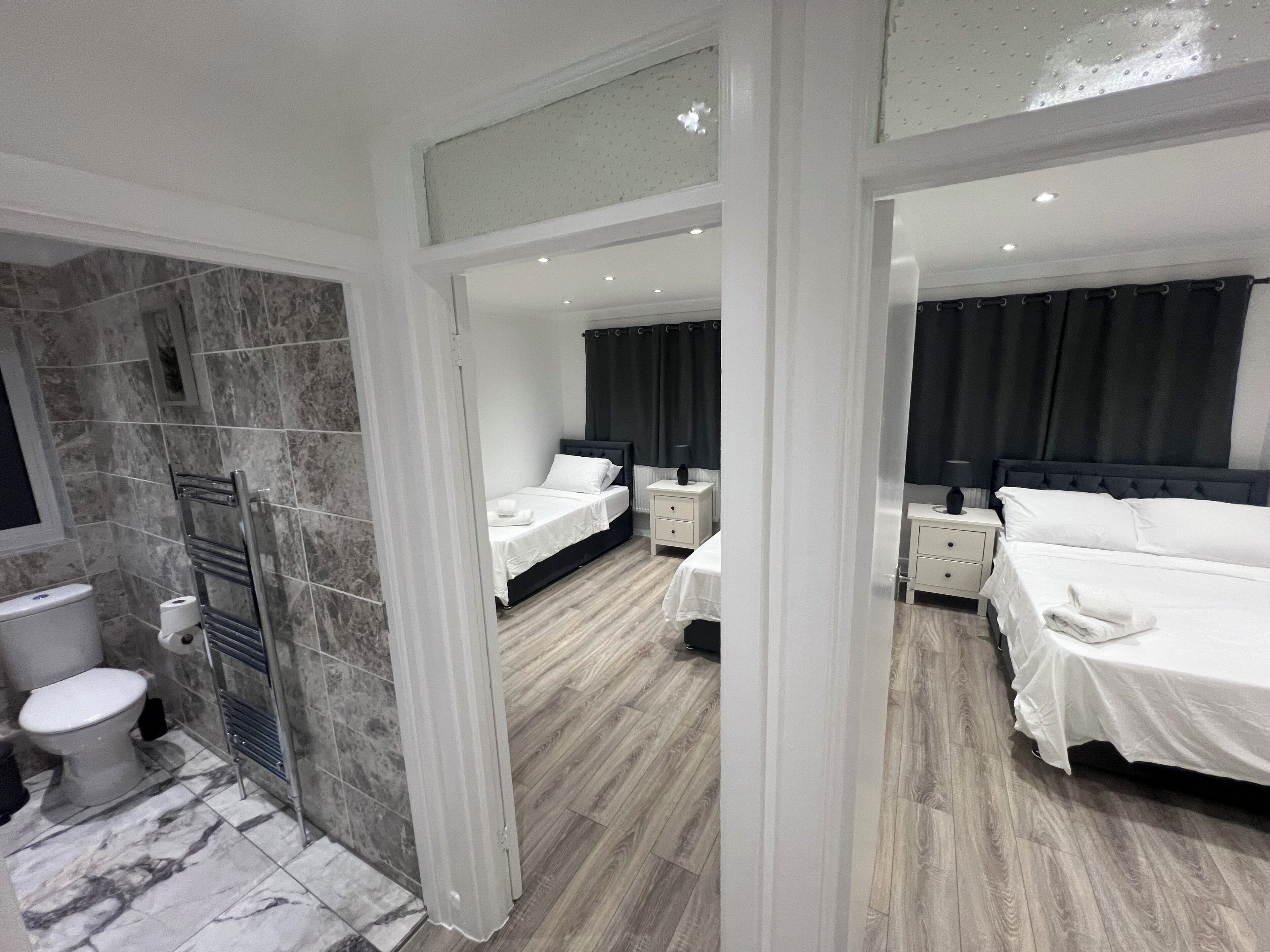 A modern hotel room with a bathroom, a double bed, a bedside table, and a nightstand.