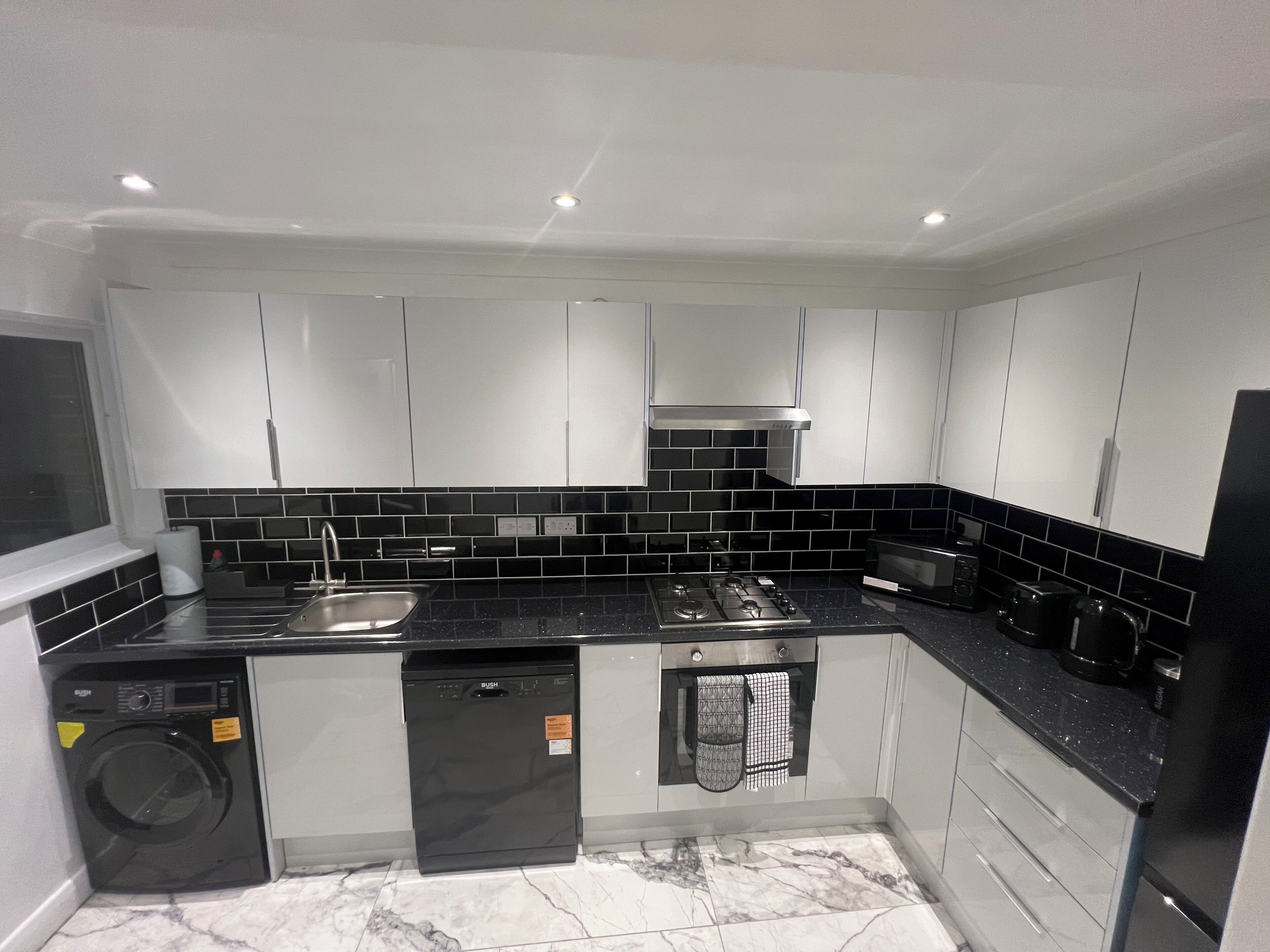 A modern kitchen with white cabinets, black countertops, a built-in dishwasher, and a stove.