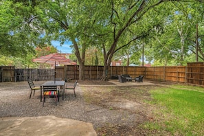 A backyard with a patio table and chairs, surrounded by a wooden fence and trees.