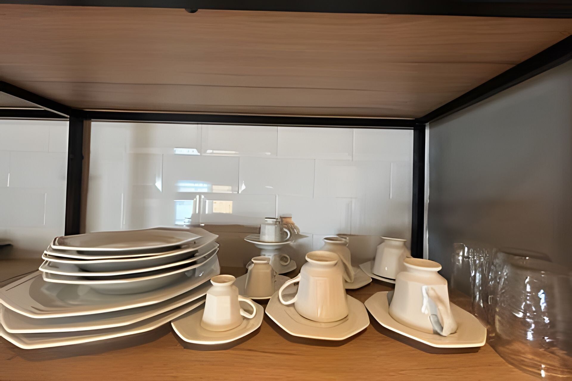 A kitchen area with white cabinets, a wooden countertop, and a stack of white plates and bowls.