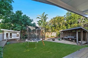 A backyard with a trampoline, a barbecue area, and a wooden structure.