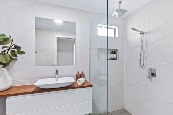 A modern bathroom with a glass shower enclosure, a white sink with a wooden countertop, and a mirror above the sink.