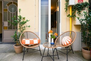 Two wicker chairs with orange and white cushions, a small table with a vase of flowers, and potted plants. - Cit Turin | Casetta Sogni (Torino)