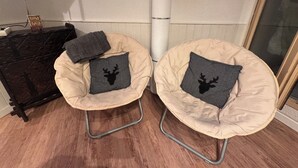 Deux fauteuils en forme de poire de couleur beige, dotés d’une structure métallique et de coussins noirs ornés de la silhouette d’un cerf, sont placés contre un mur blanc, au-dessus d’un plancher en bois.