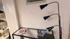 Une pièce comprenant un bureau, une chaise, un lampadaire, une affiche accrochée au mur et un porte-chaussures.