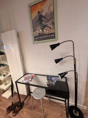 A room with a desk, a chair, a standing lamp, a poster on the wall, and a shoe rack. - Boutique Family Alpine Retreat - Skiing, Parking (Chamonix-Mont-Blanc)