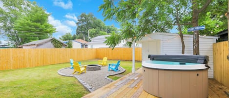 A backyard with a hot tub, wooden deck, and outdoor seating area.
