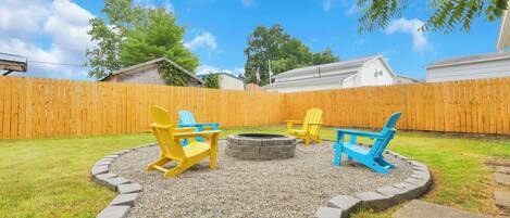 A backyard with a wooden fence, a circular fire pit, and two Adirondack chairs.