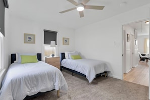 Ein Schlafzimmer mit zwei Betten, einem Deckenventilator und einer Tür zu einem weiteren Raum.